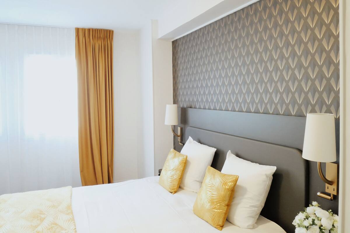 Ein Hotelzimmer mit einem großen Bett, einem gemusterten Kopfteil und einem Fenster mit Vorhängen.