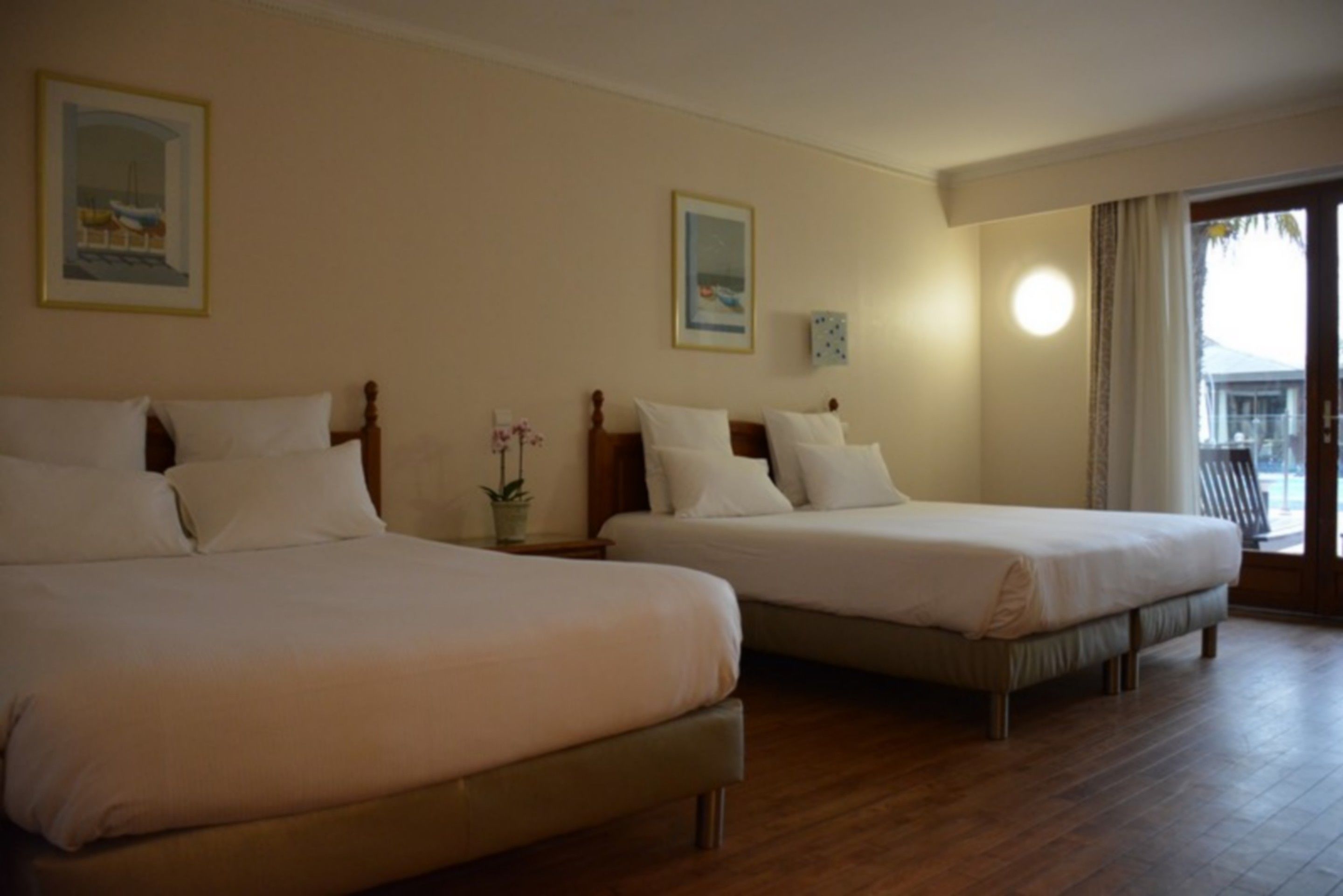 Habitación de hotel con dos camas, cabeceros de madera y un ventanal con cortinas.