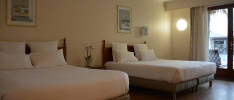 Habitación de hotel con dos camas, cabeceros de madera y un ventanal con cortinas.