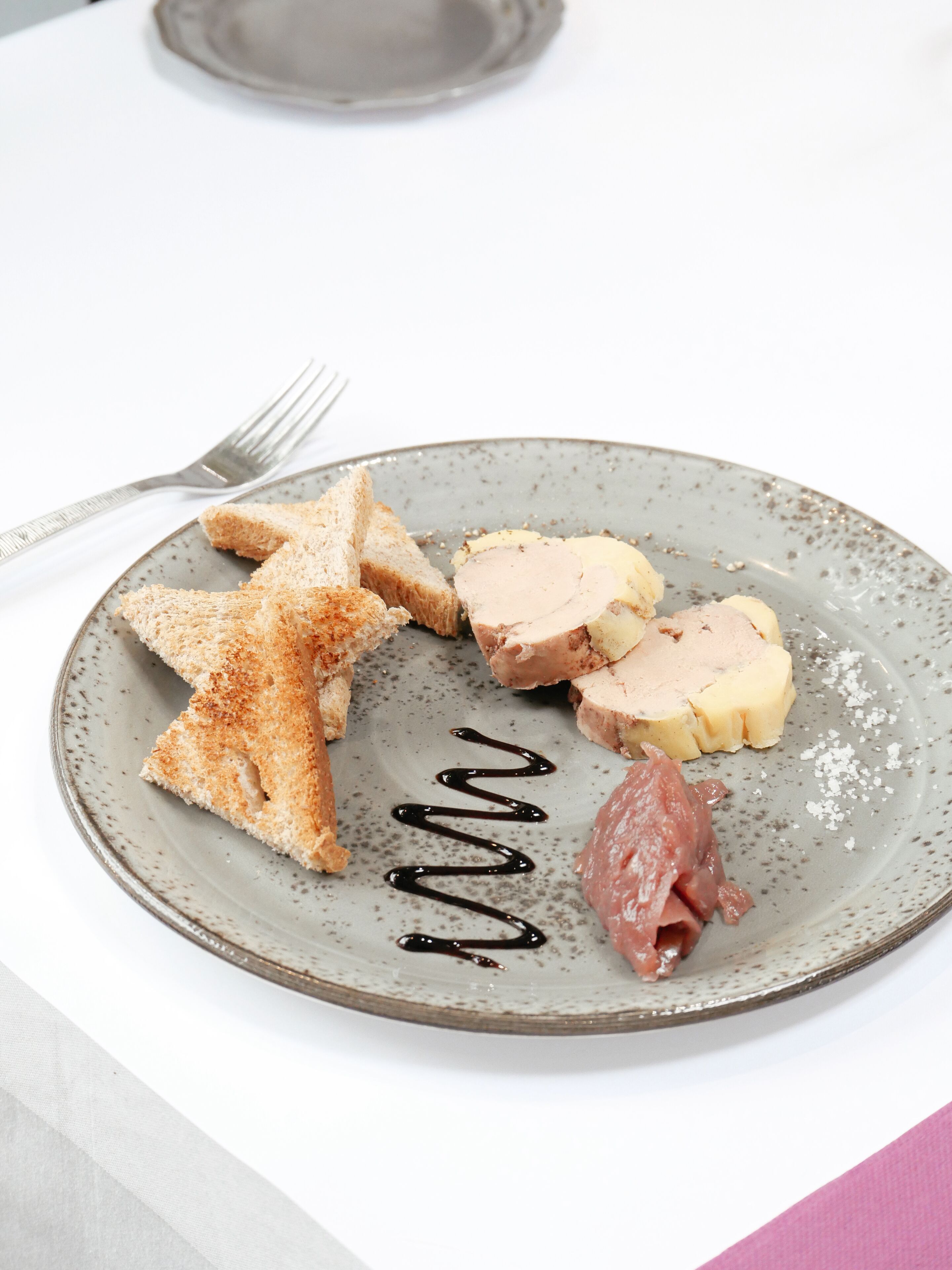 Ein Teller mit Toast, Aufschnitt und einem kleinen Stück Schinken auf einem gefleckten Keramikteller.