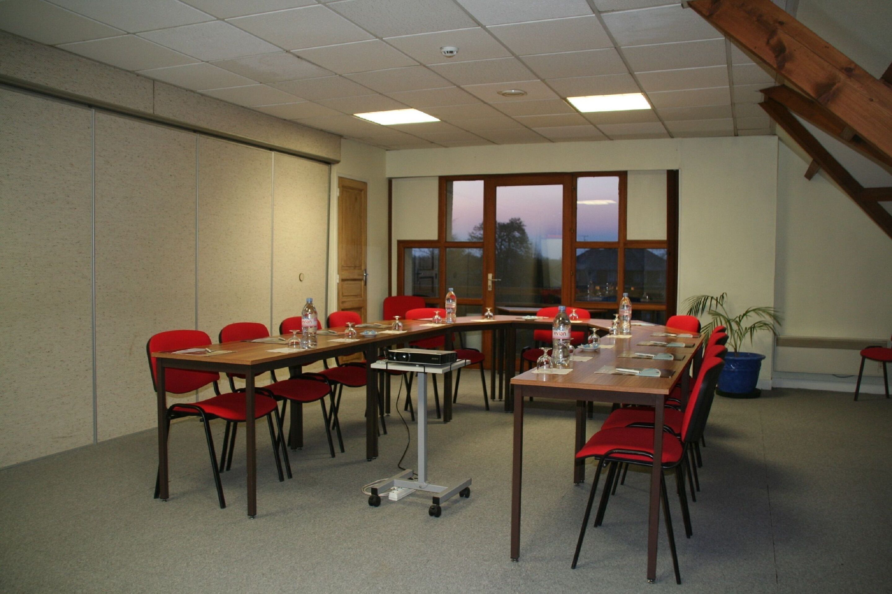A conference room with a long table, red chairs, and a projector.
