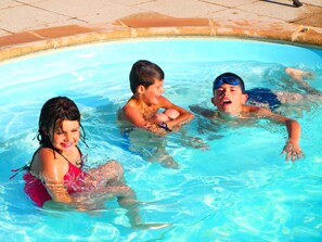 Una piscina con tres niños jugando.