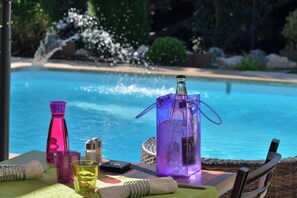 Une table avec une bouteille, des verres et un téléphone, placée près d’une piscine agrémentée d’un élément décoratif aquatique.