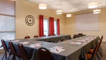 A conference room with tables, chairs, a clock, and a projector screen.