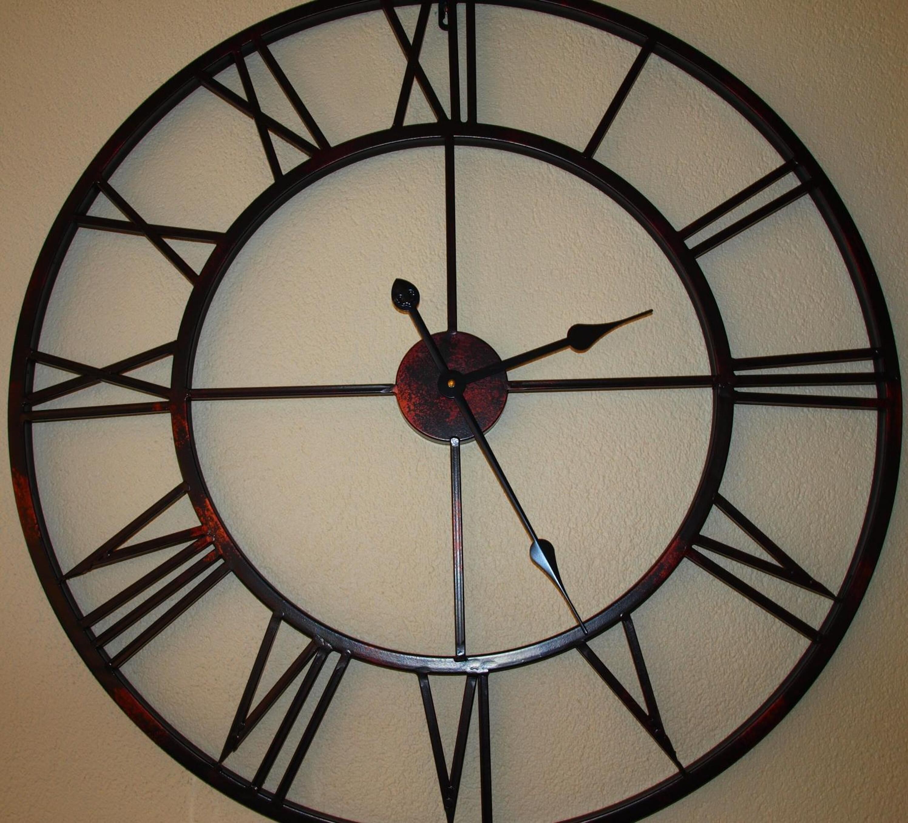 Un grande orologio a parete con numeri romani e un pendolo.