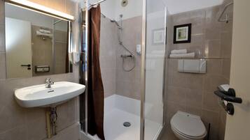 A bathroom with a shower, toilet, sink, and a framed picture on the wall.