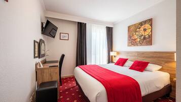 A hotel room with a large bed, a desk with a computer, a TV mounted on the wall, and a painting above the bed.