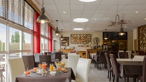 Un comedor con mesas dispuestas para el desayuno, incluyendo croissants y jugo, en un restaurante moderno con grandes ventanales y vistas al exterior.