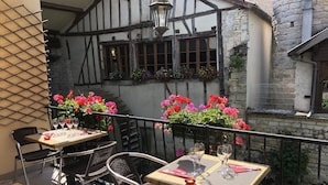 An outdoor patio with two tables and chairs, each set with wine glasses and cutlery, surrounded by a lattice fence and flowering plants.