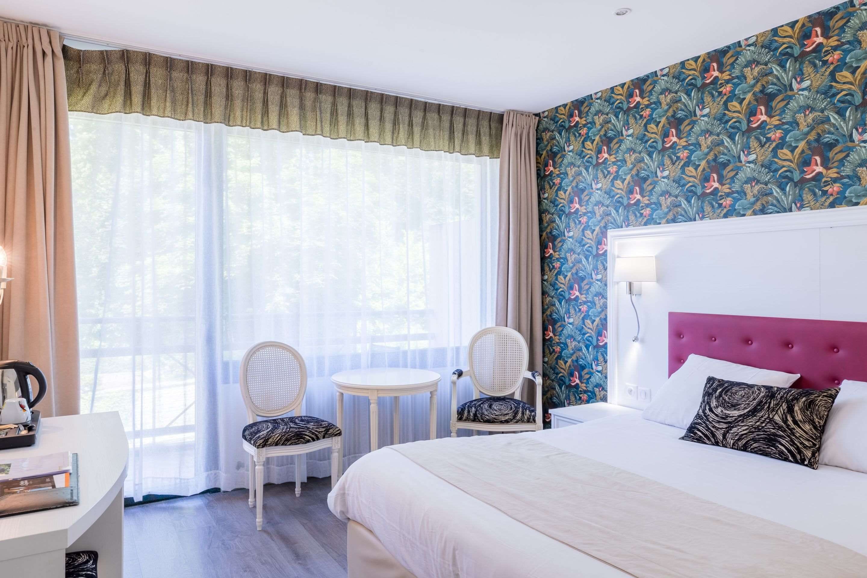 Habitació d'hotel amb un llit, dues cadires, una taula petita, un escriptori i una finestra amb cortines.