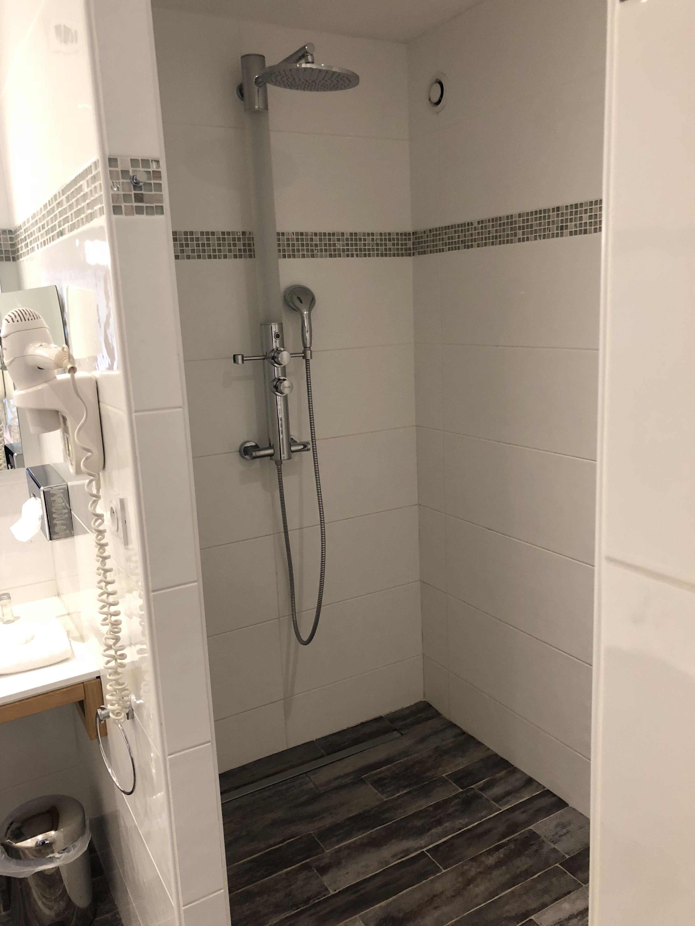A small, tiled shower room with a showerhead, handheld shower, and a toilet.
