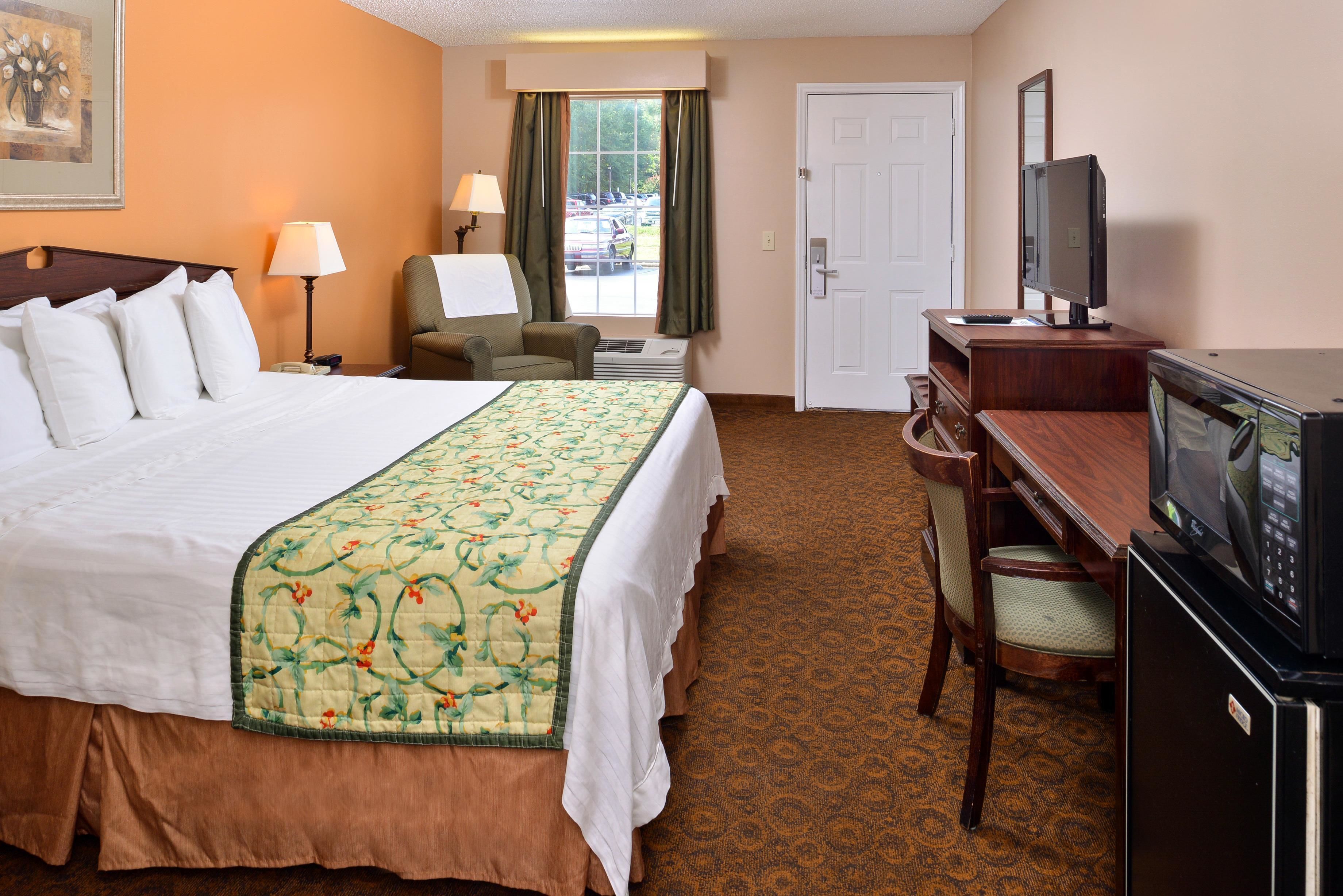 A hotel room with a large bed, a desk with a television, a chair, and a window with curtains.