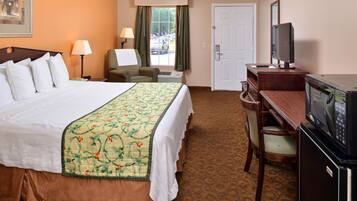 A hotel room with a large bed, a desk with a television, a chair, and a window with curtains.