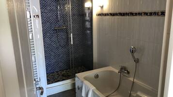 A bathroom with a shower area featuring a black and white mosaic tile wall, a white bathtub with a showerhead, and a towel hanging on the side.