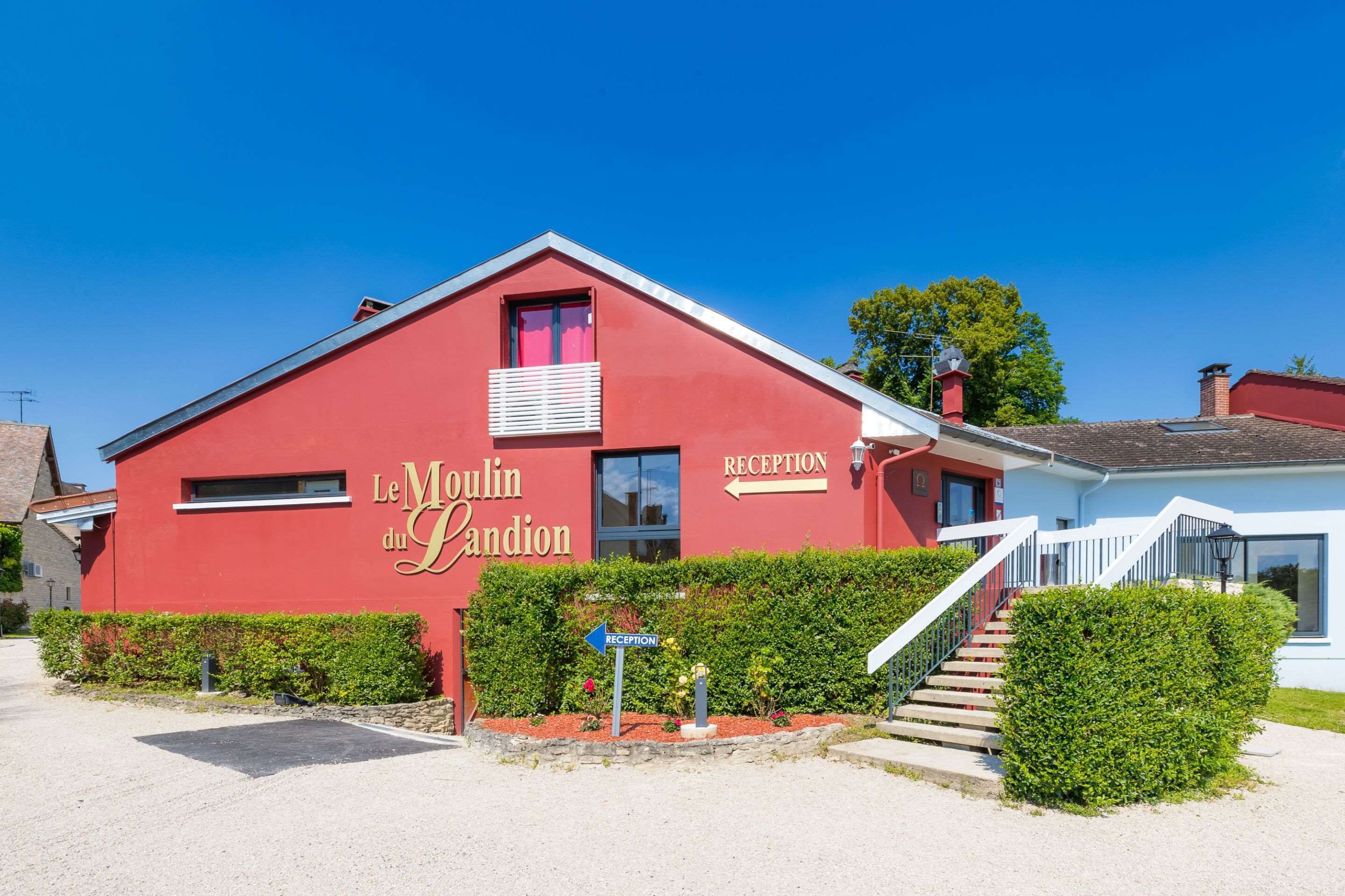 A red building with a reception sign, a staircase, and a hedge in front.