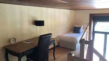 Ein Zimmer mit einem Holztisch, einem Stuhl, einem Bett mit Kissen, einer Lampe und einem Fenster.