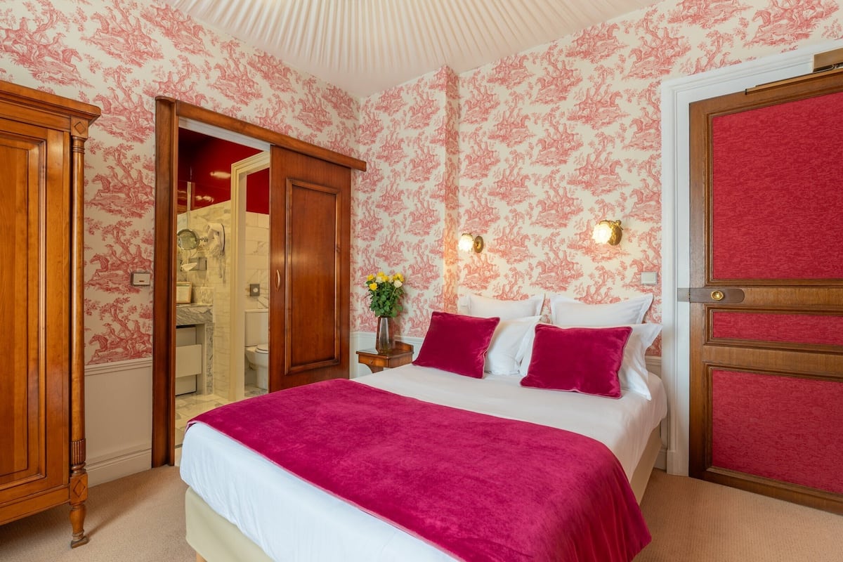 A bedroom with a large bed, wooden wardrobe, and a mirror.