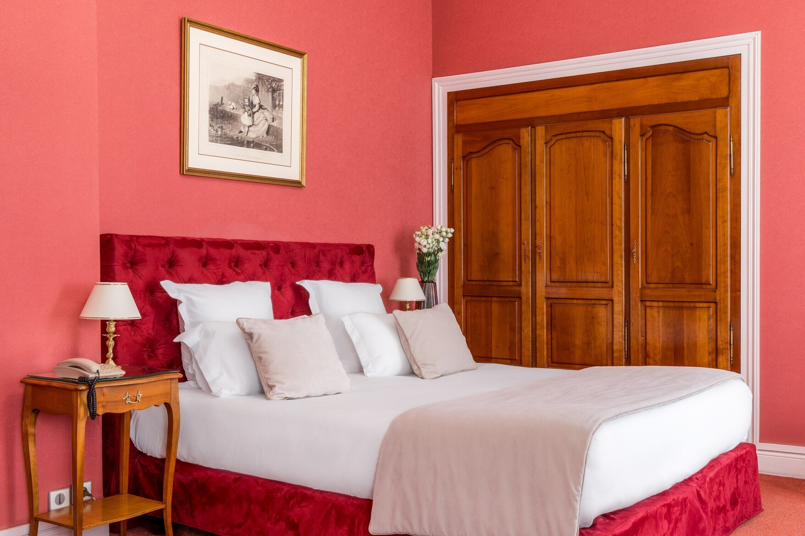 Una camera da letto con testiera imbottita rossa, un letto bianco, un comodino in legno con una lampada e un'ampia armadio in legno.