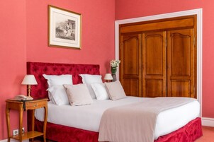 Una camera da letto con testiera imbottita rossa, un letto bianco, un comodino in legno con una lampada e un'ampia armadio in legno.