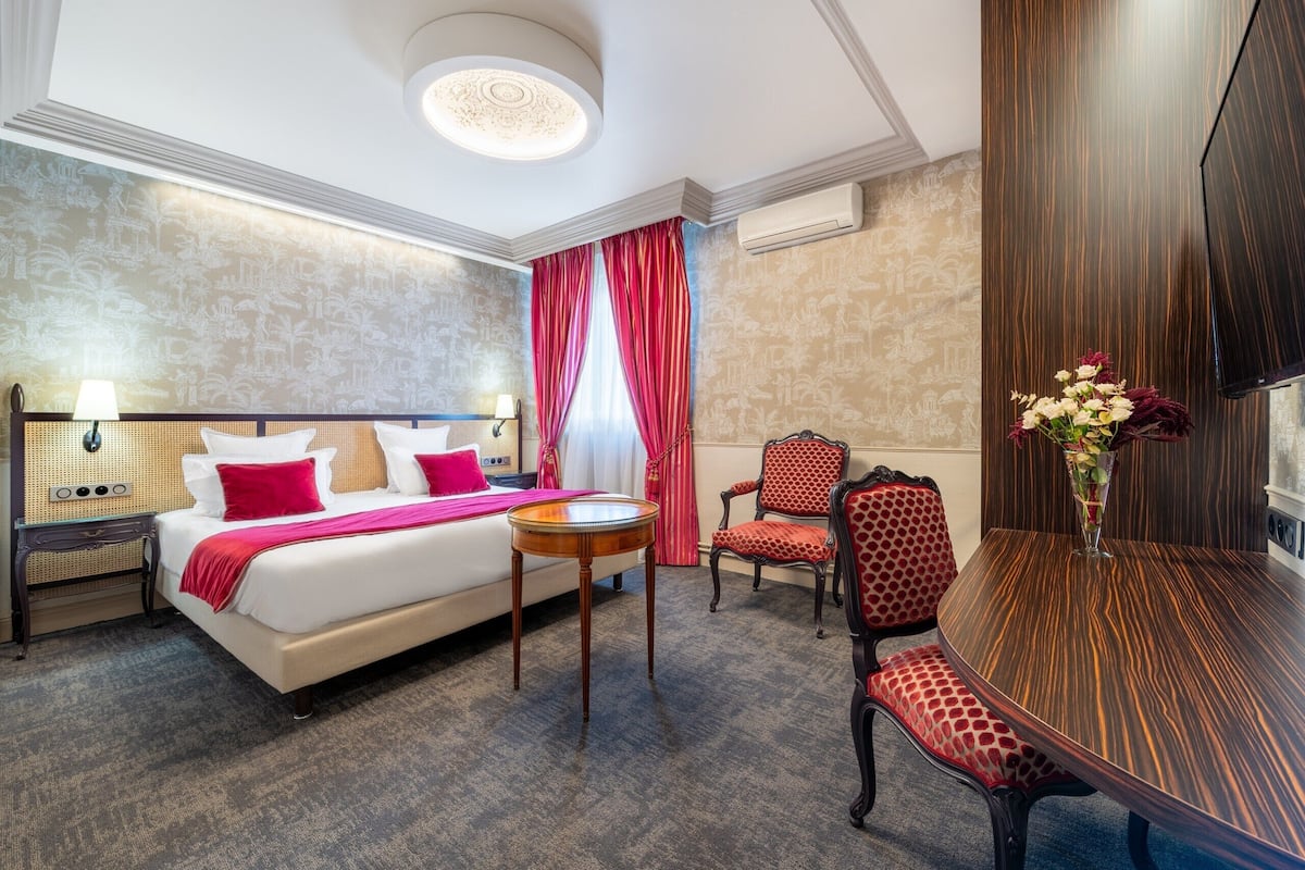 A hotel room with a bed, a round table, two chairs, a TV, and a decorative vase.