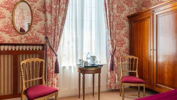 Habitación de hotel con dos sillas de madera, una mesita redonda con una tetera, un radiador y un armario.