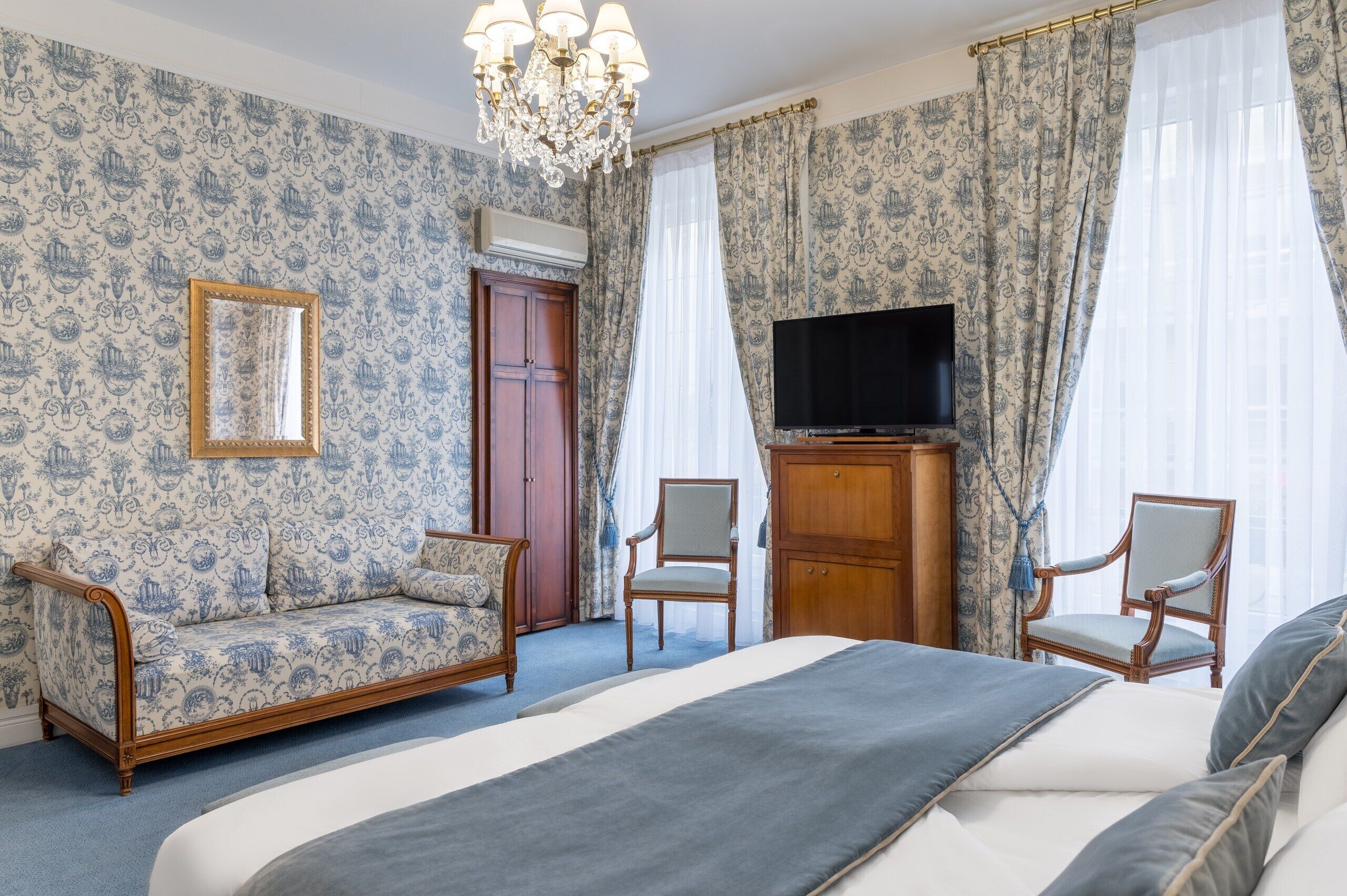 Une chambre à coucher comprenant un lit, deux fauteuils, une armoire en bois, un téléviseur et un lustre.