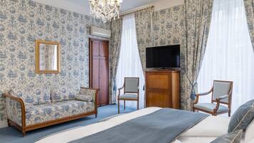 Un dormitorio con una cama, dos sillones, un armario de madera, un televisor y una araña.