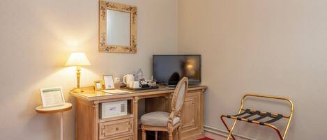 Habitación de hotel con un escritorio de madera, una silla, un televisor, una lámpara, un espejo y un perchero metálico.