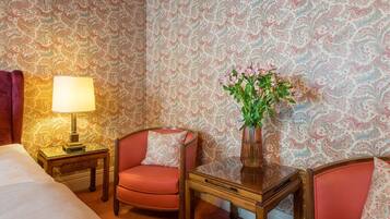 Een hotelkamer met behang met een patroon, een bed, een stoel, een tafel en een lamp.