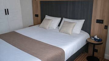 A neatly made bed with a wooden headboard, a bedside table with a lamp, and a wooden floor.