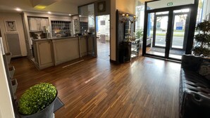 A hotel lobby with a reception desk, a kitchen area, and a seating area with a potted plant. - The Originals City, Hôtel Napoléon, La Roche-sur-Yon (La Roche-sur-Yon)
