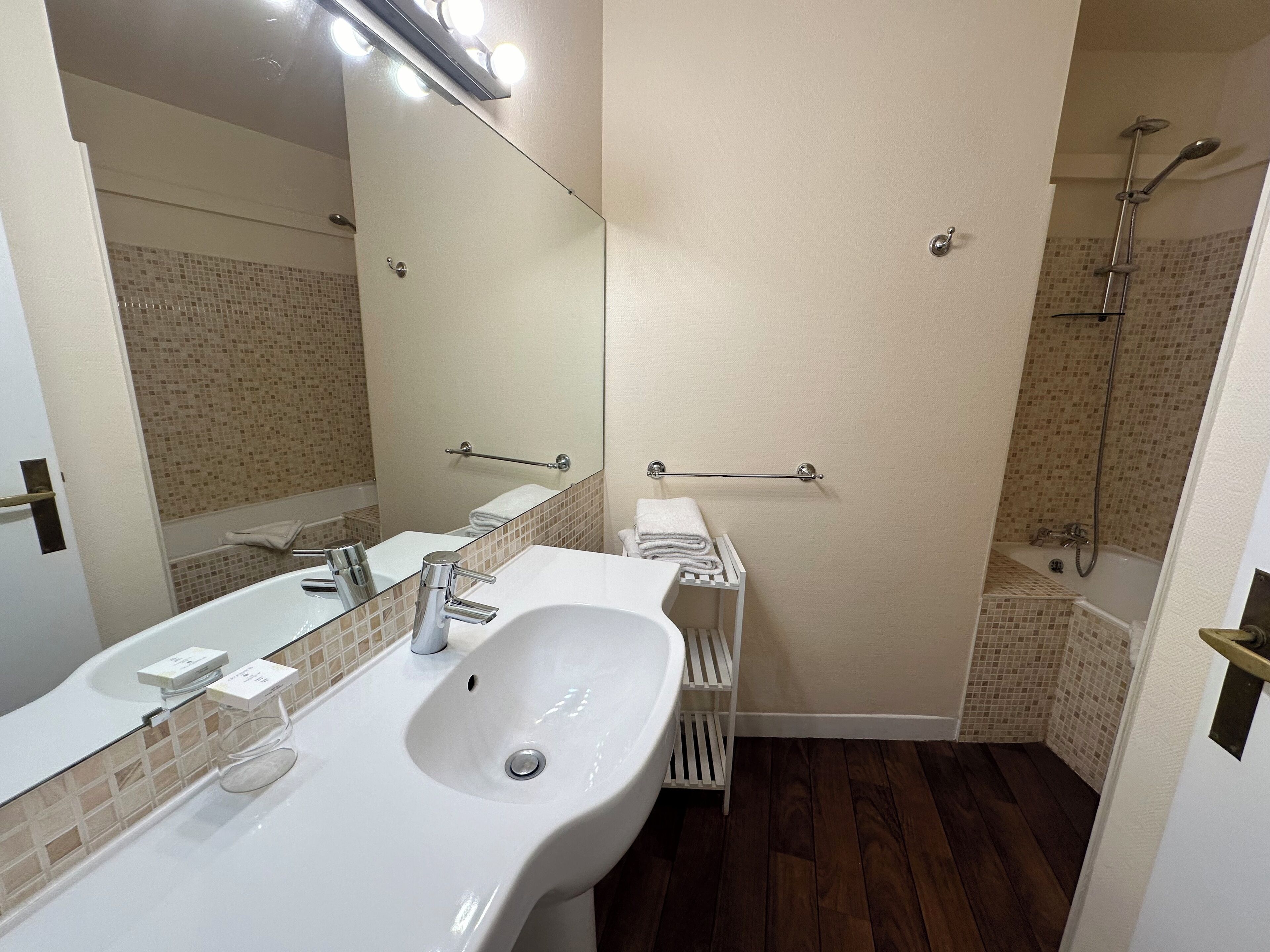 A bathroom with a large mirror, two sinks, a shower, and a towel rack.