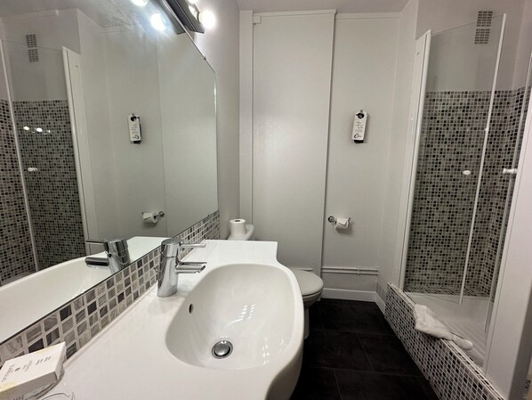 A bathroom with a white sink, a mirror, a toilet, and a shower area.