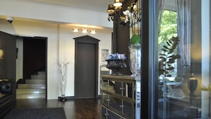 A modern interior with a staircase, a dark-colored sofa, a glass display cabinet, and a large window with natural light. - The Originals City, Hôtel Napoléon, La Roche-sur-Yon (La Roche-sur-Yon)