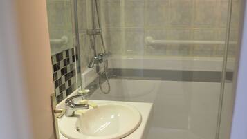A bathroom with a glass-enclosed shower, a sink with a mirror, and a tiled floor.