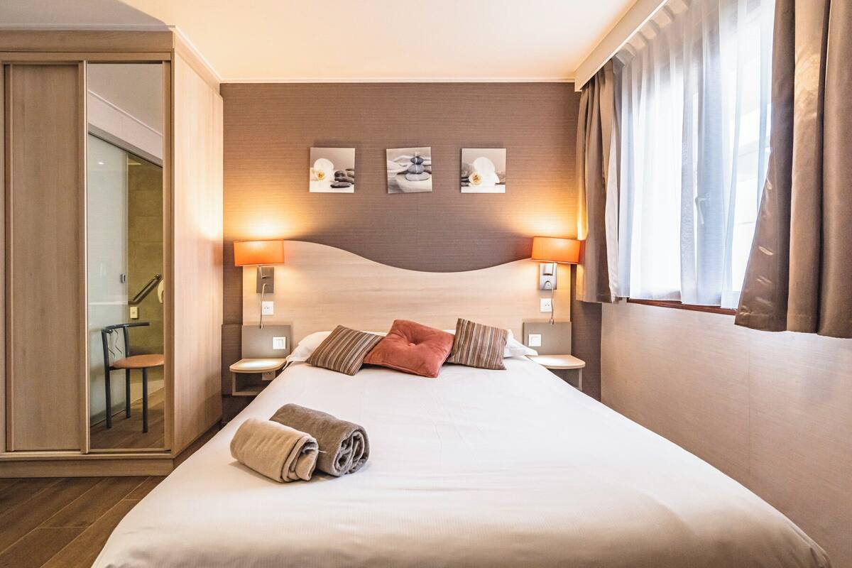 A hotel room with a large bed, two bedside lamps, and three wall-mounted artworks.