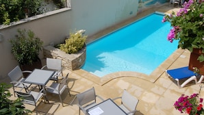 A swimming pool with a tiled deck, surrounded by outdoor seating and potted plants. - Logis Hôtel Au Tambour (Reims)