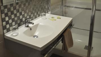 A modern bathroom with a large mirror, a white sink, a glass shower enclosure, and a towel hanging on the wall.