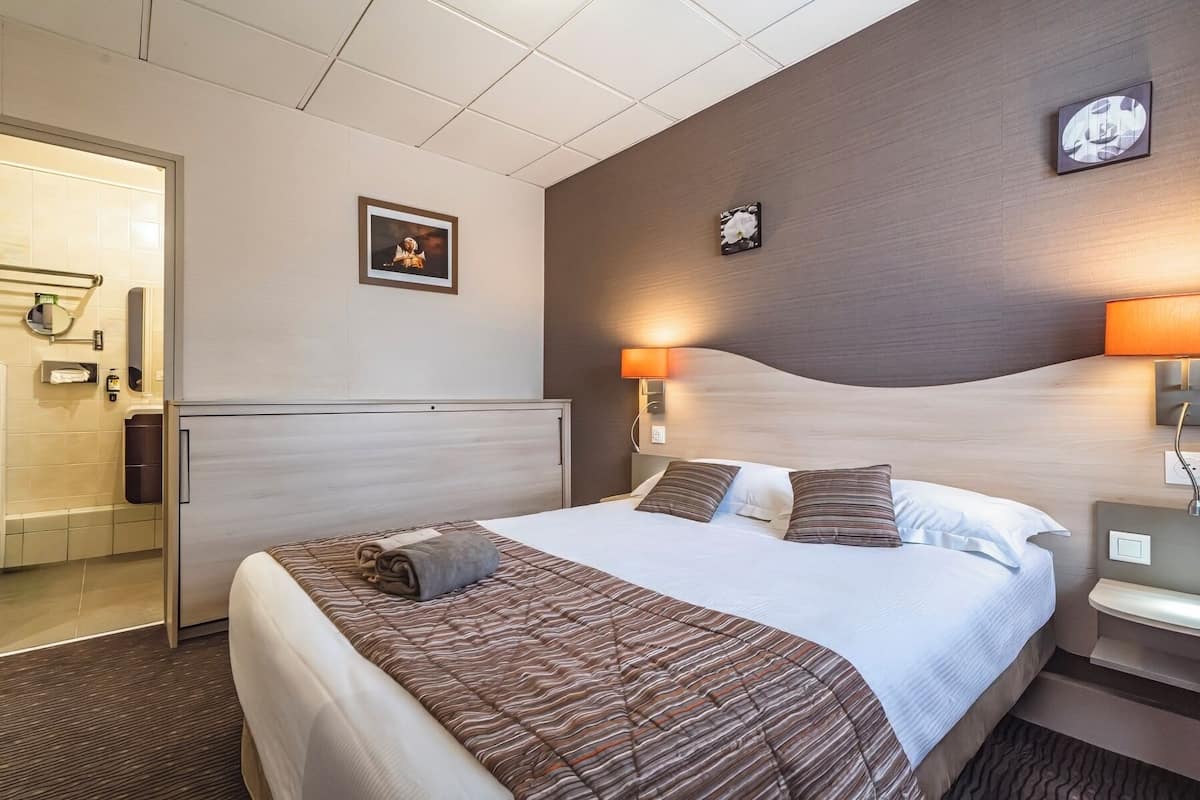 A hotel room with a large bed, a headboard, a bedside table, a lamp, and a framed picture on the wall.