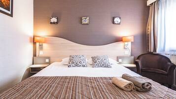 Una habitación de hotel con una cama grande, dos lámparas de noche, una silla y tres relojes en la pared.