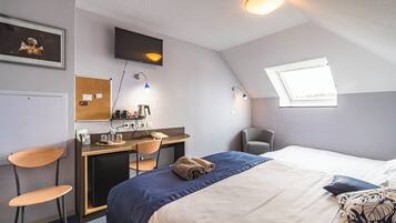A bedroom with a bed, desk, chairs, a television, a window, and a skylight.