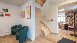 A modern interior with a staircase, green seating area, and a dining space with patterned wallpaper. - Logis Hôtel Au Tambour (Reims)