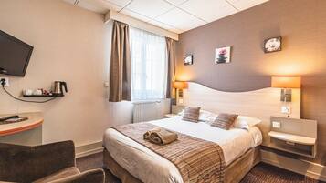A hotel room with a bed, bedside tables, a desk with a coffee maker, a TV, and a window with curtains.