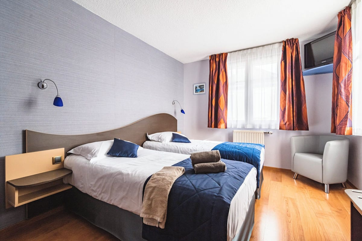 A hotel room with two beds, a TV, a desk, and a chair.