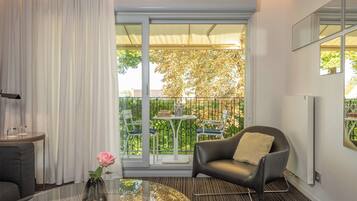 A modern living room with a glass table, a leather armchair, and a view of a balcony with outdoor furniture.