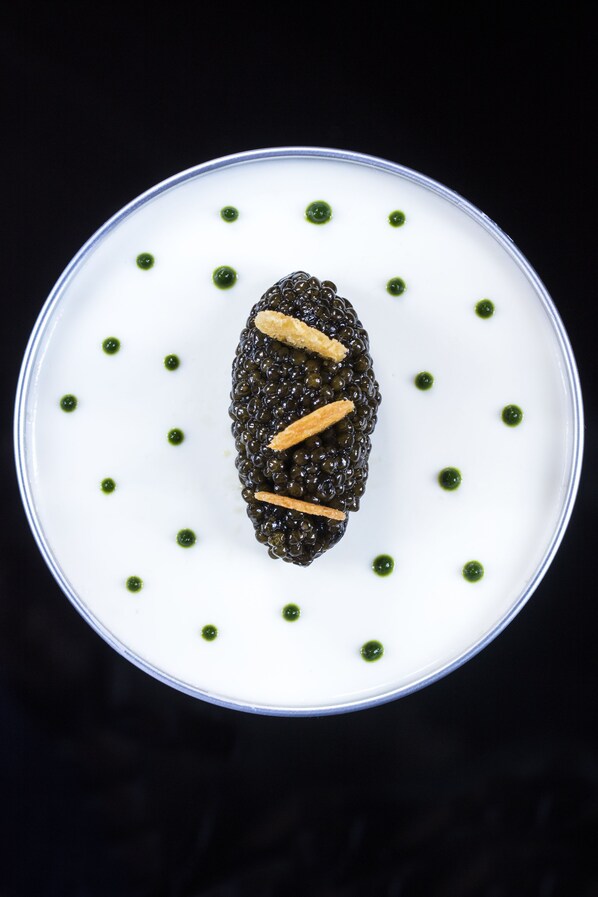 Un postre con caviar negro y esferas verdes sobre un plato blanco.