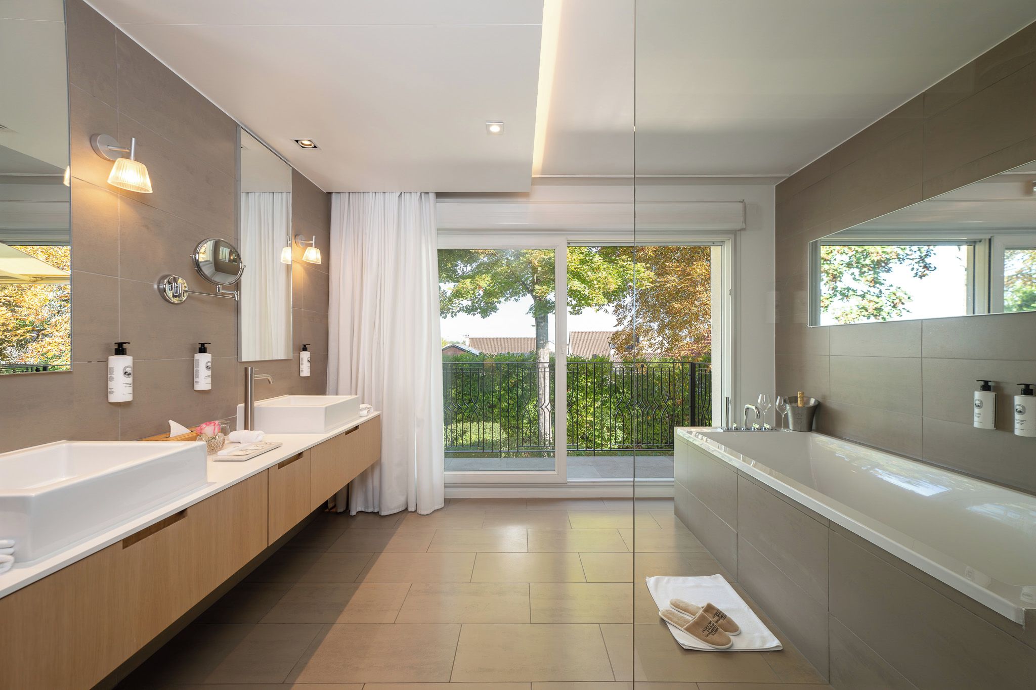 A modern bathroom with dual sinks, a large mirror, and a view of the outdoors through a sliding glass door.
