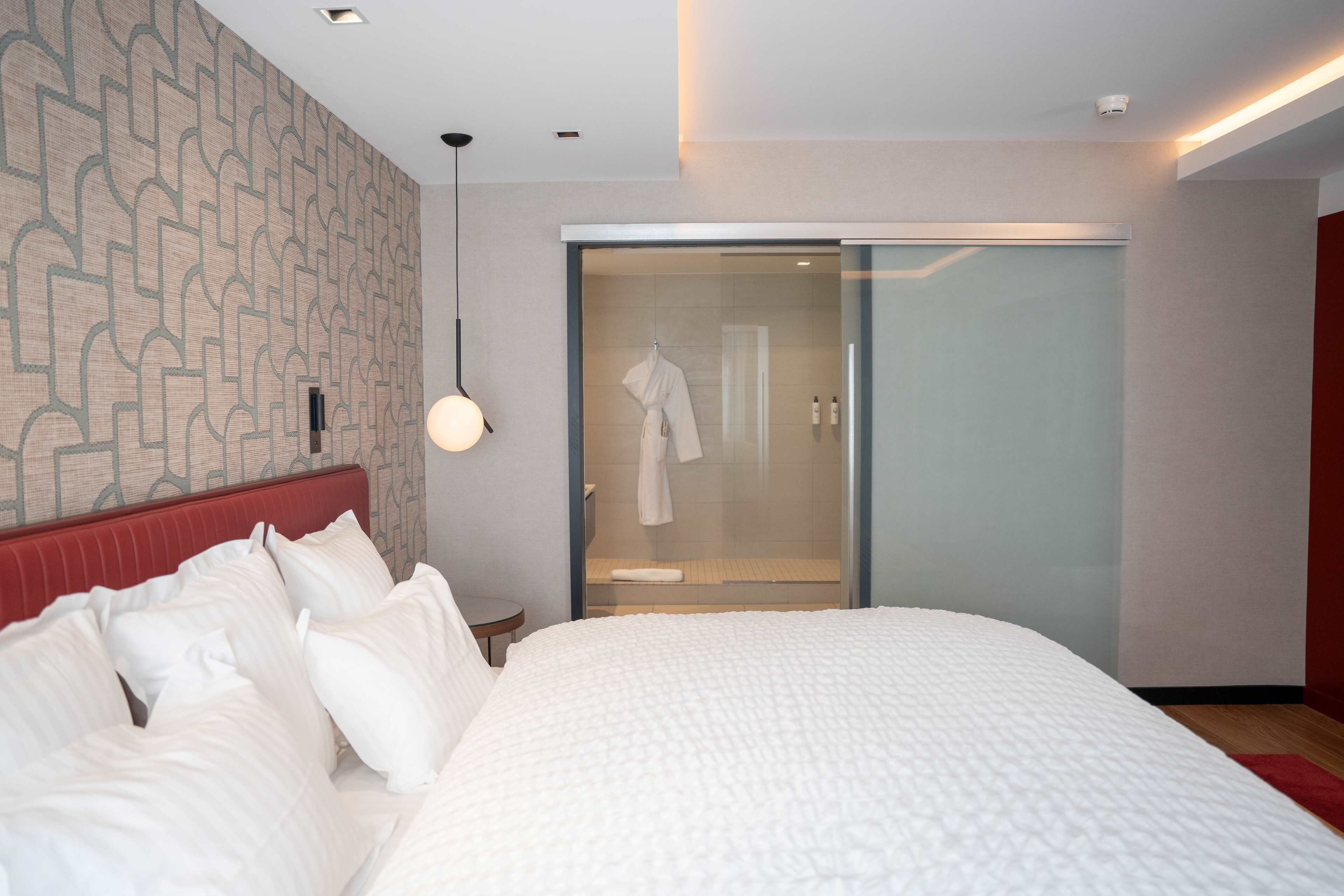 A modern hotel room with a large bed, a glass-enclosed shower, and a patterned wall.