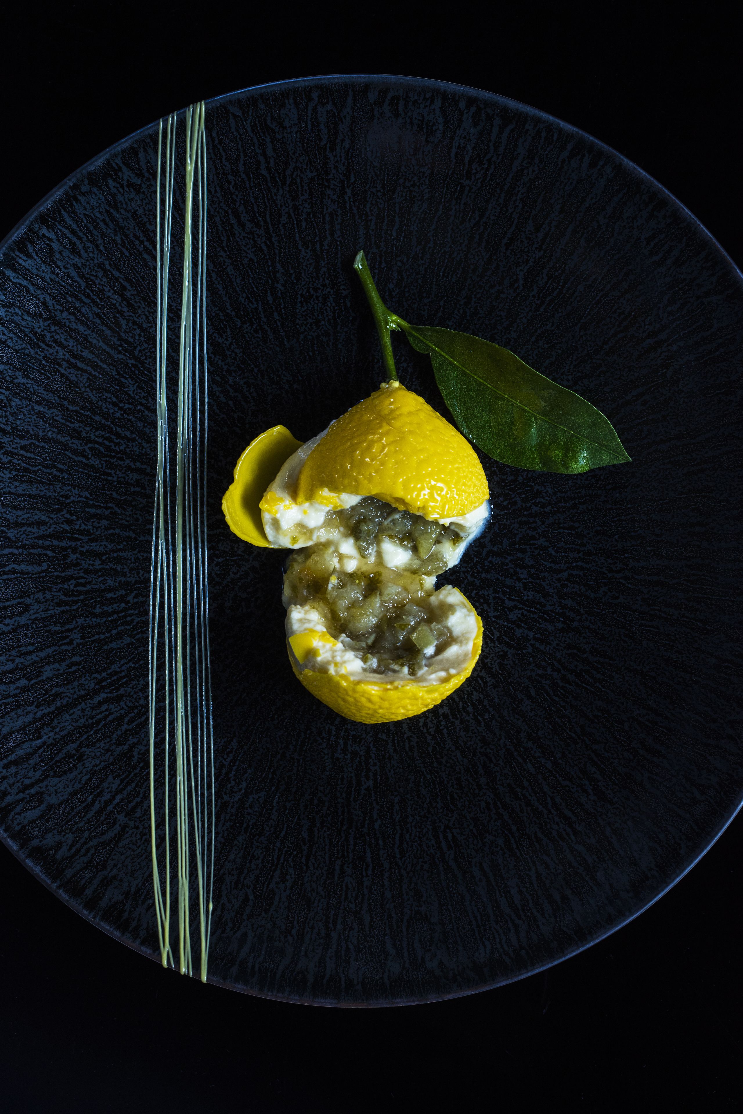 En mørkeblå tallerken med et citron og et grønt blad.