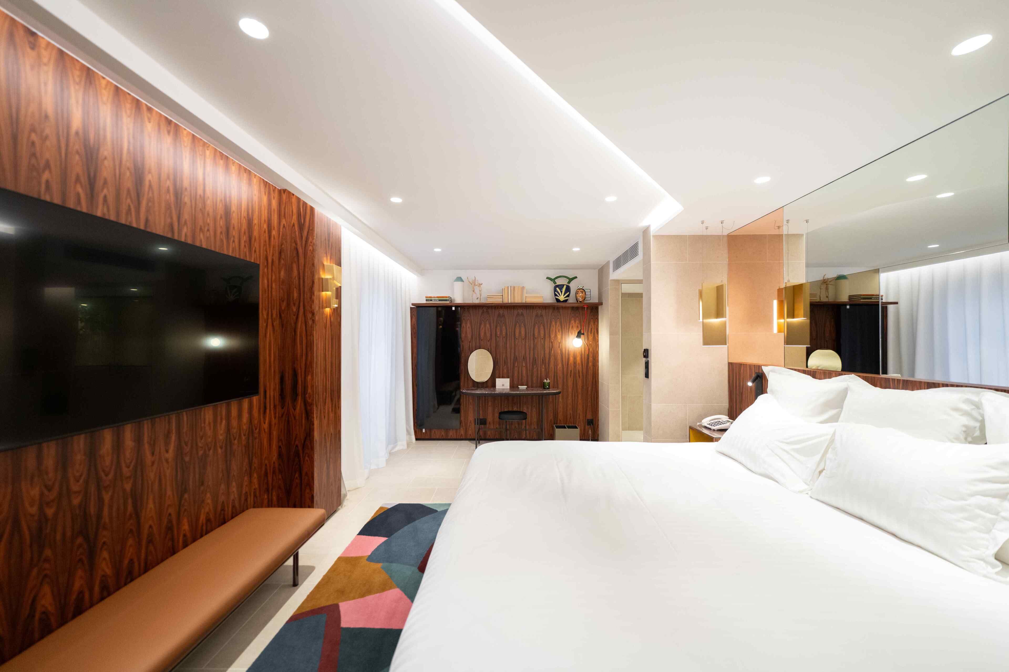 Une chambre d’hôtel moderne équipée d’un grand lit, d’une banquette, d’une télévision, d’un bureau et d’un miroir.